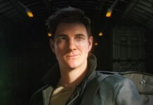Young man with a backpack gazing upward in a dark, industrial-looking hangar or warehouse setting.