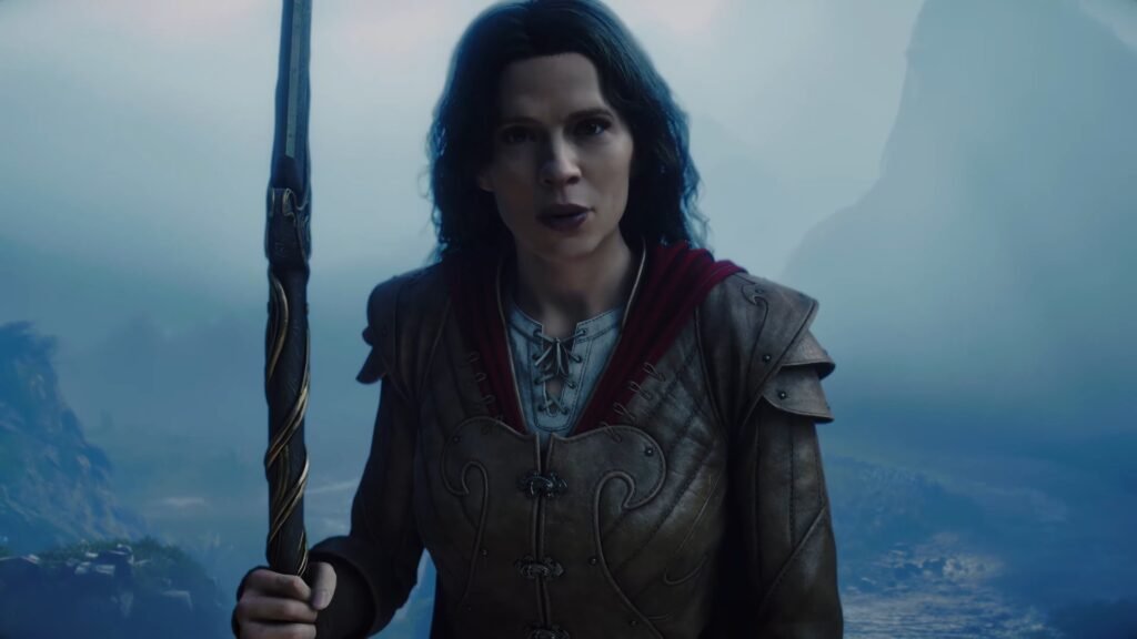 Fable - Official Release Date Trailer _ Xbox Games Showcase 2026 2-13 screenshot - GamersPack ישראל Female warrior in brown armor grips a carved staff, standing on a cliff with a blue misty landscape behind her. Fable - Official Release Date Trailer _ Xbox Games Showcase 2026 2-13 screenshot