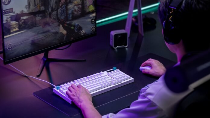 Gamer wearing a headset using a white keyboard and mouse, playing a shooter on a large monitor with neon purple lighting.