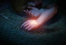 Hands resting on a woven mat with a glowing Triforce-like triangle on the wrist in dim light