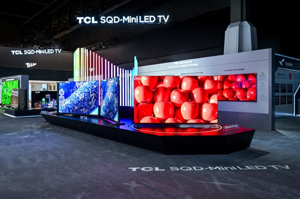 X11L קרדיט צילום TCL2 - GamersPack ישראל TCL booth at a tech expo with multiple SQD-Miniled TV displays and a curved screen showing red fruit imagery. X11L קרדיט צילום TCL2