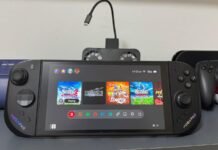 ביקורת MOBAPAD M12S: הג'ויקונים שהפכו את ה-Switch 2 לנוח יותר Nintendo Switch OLED in handheld mode on a desk, displaying the home screen with game icons and two controllers on either side.