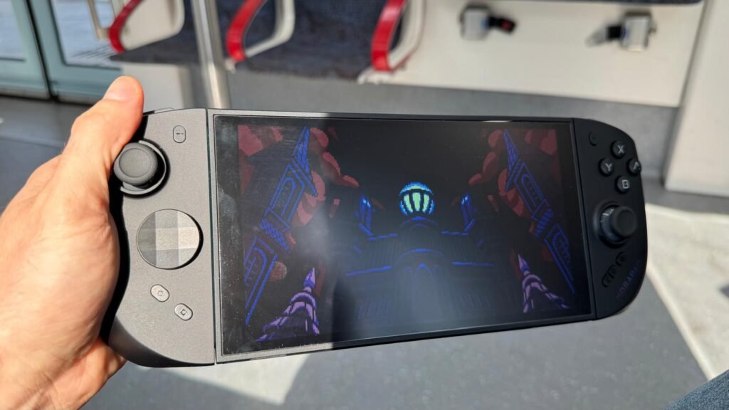 WhatsApp Image 2026-08-23 at 155502 - GamersPack ישראל Person holds a handheld gaming console, screen shows a dark cathedral scene with blue neon lights from a game. WhatsApp Image 2026-08-23 at 155502