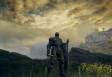 Fully armored knight with shield and red sword stands on a grassy hill, gazing at rocky cliffs under a golden, cloudy sky.