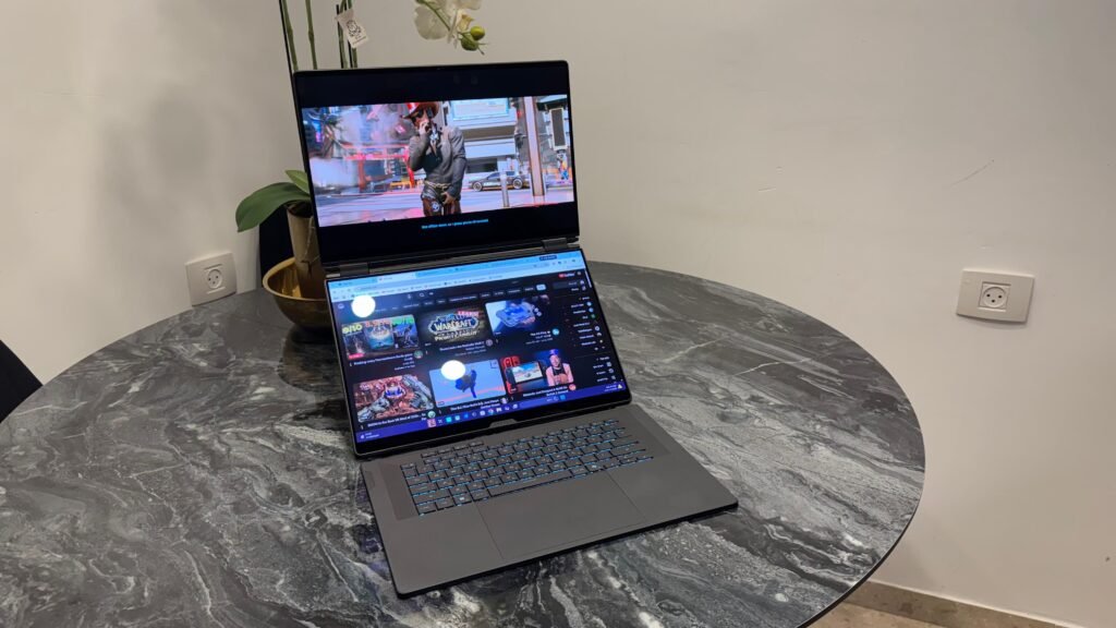 Laptop on a marble round table showing a video on the top screen; a plants pot sits behind it and a wall with outlets to the right. WhatsApp Image 2026-09-22 at 112536