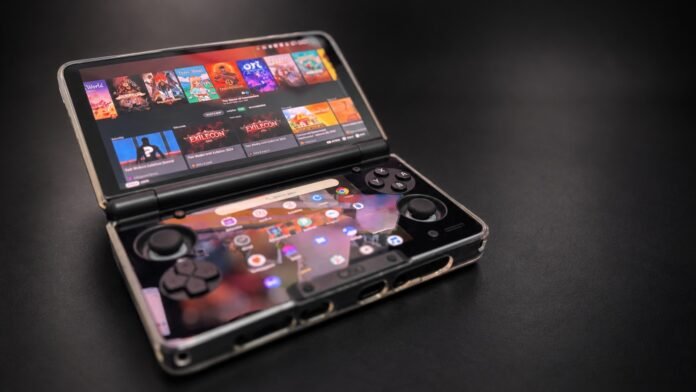 Foldable handheld gaming console open on a dark surface, showing colorful game icons on the top screen and control buttons below.