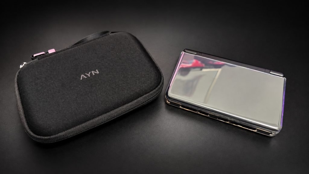 WhatsApp Image 2026-10-27 at 192154 - GamersPack ישראל Black zippered carrying case with an AYN logo beside a glossy handheld gaming device on a dark surface. WhatsApp Image 2026-10-27 at 192154